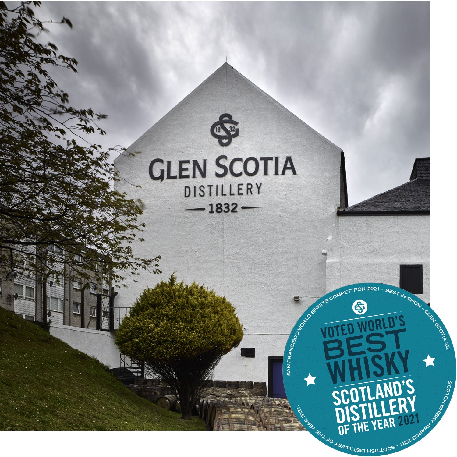 A white building with "Glen Scotia Distillery 1832" written on the side, surrounded by greenery. A circular blue badge in the bottom right corner reads, "Voted World's Best Whisky - Scotland’s Distillery of the Year 2021.